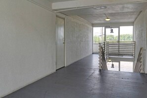 An empty hallway with a door on the left, a staircase with metal railings on the right, and a large window at the end. - 2 Queen Beds | NSMK, Micfridge (Sacramento CA)