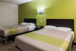 Une chambre d’hôtel avec deux lits simples, une table de chevet avec un téléphone et un luminaire fixé au mur.