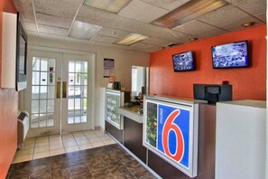 Un espace d’accueil comprenant un comptoir, deux écrans, un grand panneau portant le chiffre « 6 » et une porte donnant sur l’extérieur.