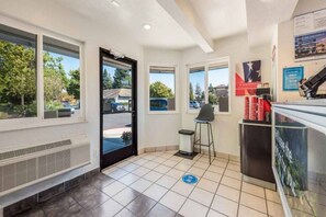 A hotel reception area with a tiled floor, a trash bin, a chair, and a counter with a coffee machine. - 2 Full Beds | Deluxe, Micfridge (Sacramento CA)