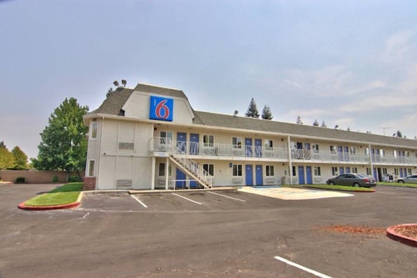 Een motel met een 6 logo, meerdere verdiepingen, een parkeerplaats en een kleine tuin.