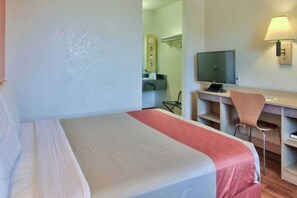 Ein Hotelzimmer mit einem Bett, einem Schreibtisch mit Stuhl, einem Fernseher und einer Lampe.