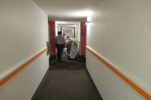 A hotel corridor with a carpeted floor, white walls, and orange trim. - Elegant 1 Queen Bed | Mini Fridge (Sacramento CA)