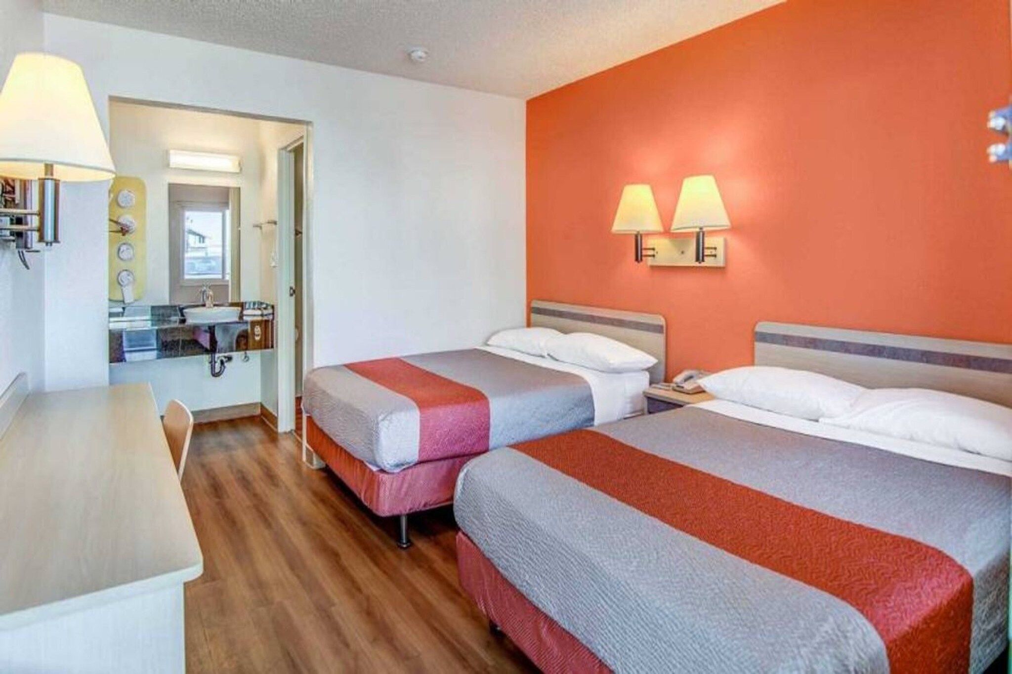 A hotel room with two beds, a desk, and a bathroom visible through an open door.