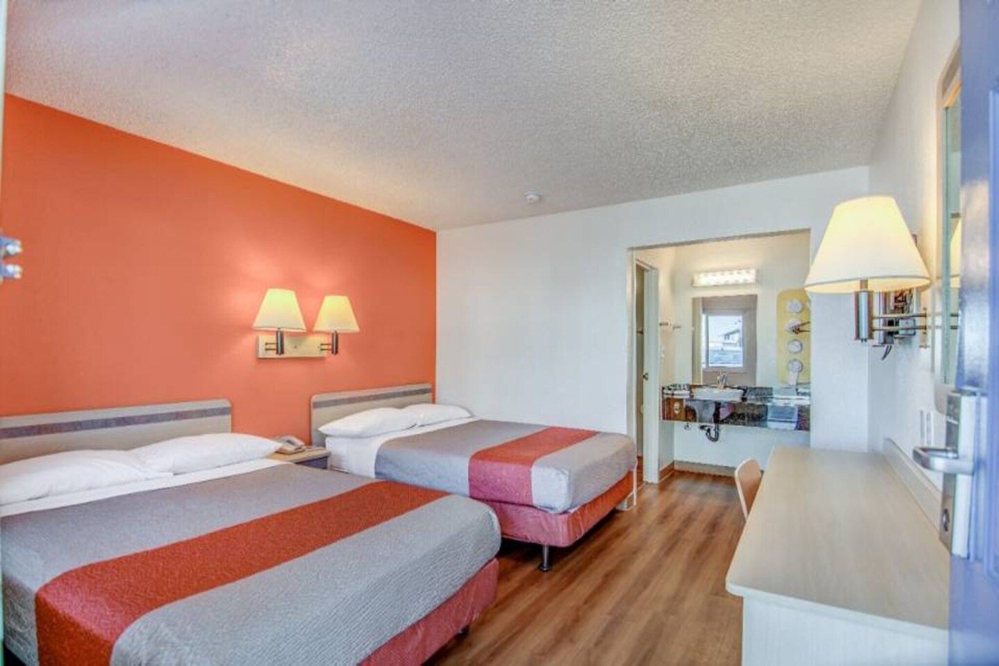 Habitación de hotel con dos camas, un escritorio y un baño visible a través de una puerta abierta.