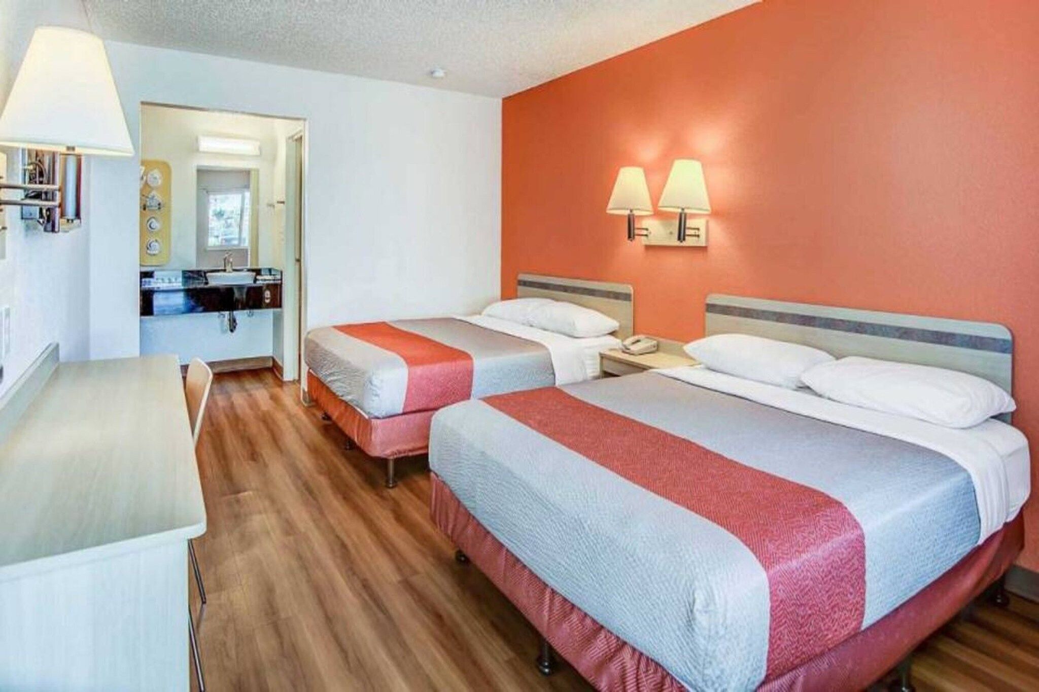 Une chambre d’hôtel avec deux lits, un bureau et une salle de bain visible à travers une porte ouverte.