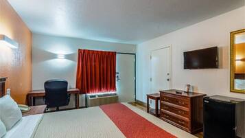 A hotel room with a bed, a desk, a chair, a dresser, a television, and a window with curtains.