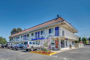 A motel with a red-tiled roof, multiple windows, and a parking lot with several cars.