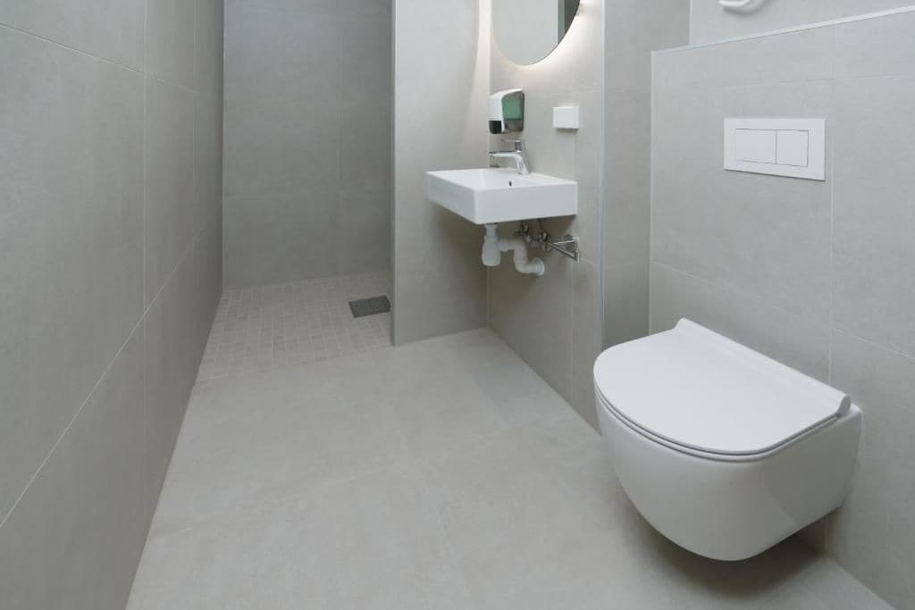 Et moderne badeværelse med toilet, vask med spejl og vægmonteret lysarmatur.