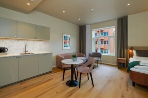 Una habitación de hotel moderna con cocina, una mesa de comedor con sillas, un sofá y una cama.