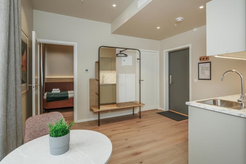 Habitació d'hotel moderna amb terra de fusta, una taula rodona per dinar, una petita planta en test, un llit amb llençol verd, un mirall, una cadira penjant, un banc integrat, un lavabo i una porta que condueix a un bany.