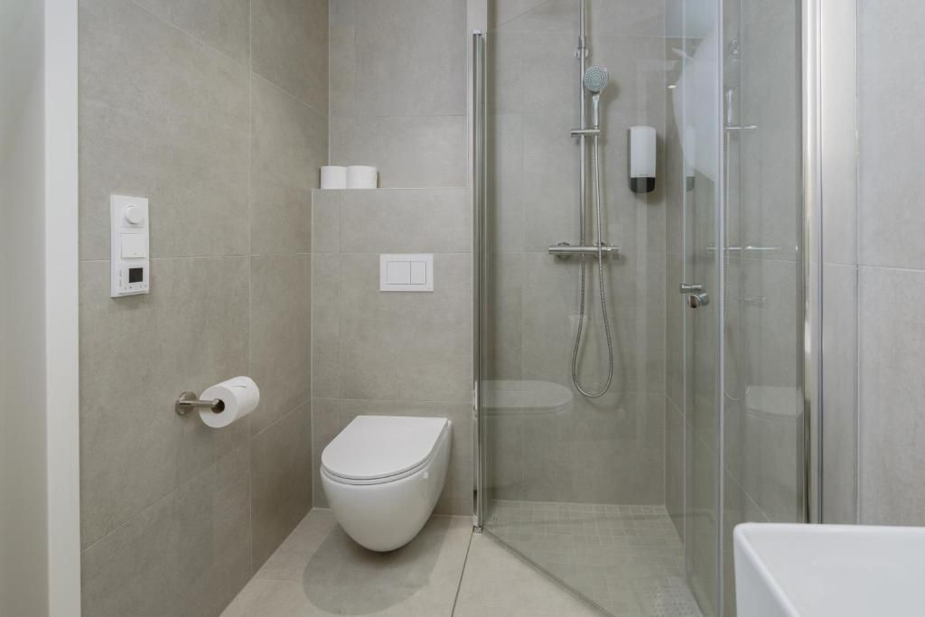 Un baño moderno con inodoro, cabina de ducha y dispensador de papel higiénico.