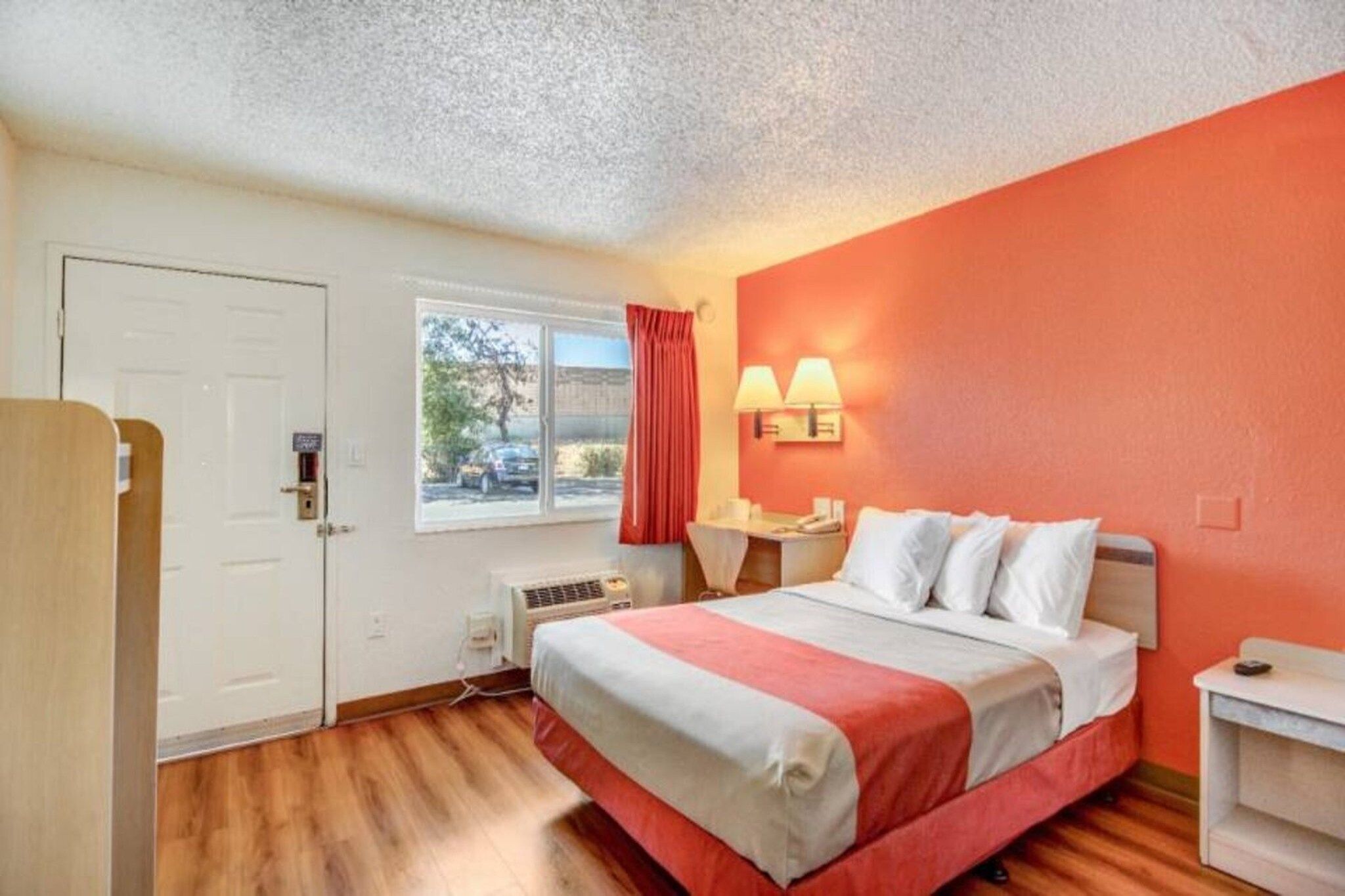 Ein Hotelzimmer mit Bett, Schreibtisch, Stuhl, einem Fenster mit Vorhängen und einer Tür.