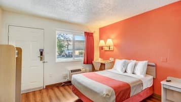 A hotel room with a bed, a desk, a chair, a window with curtains, and a door.