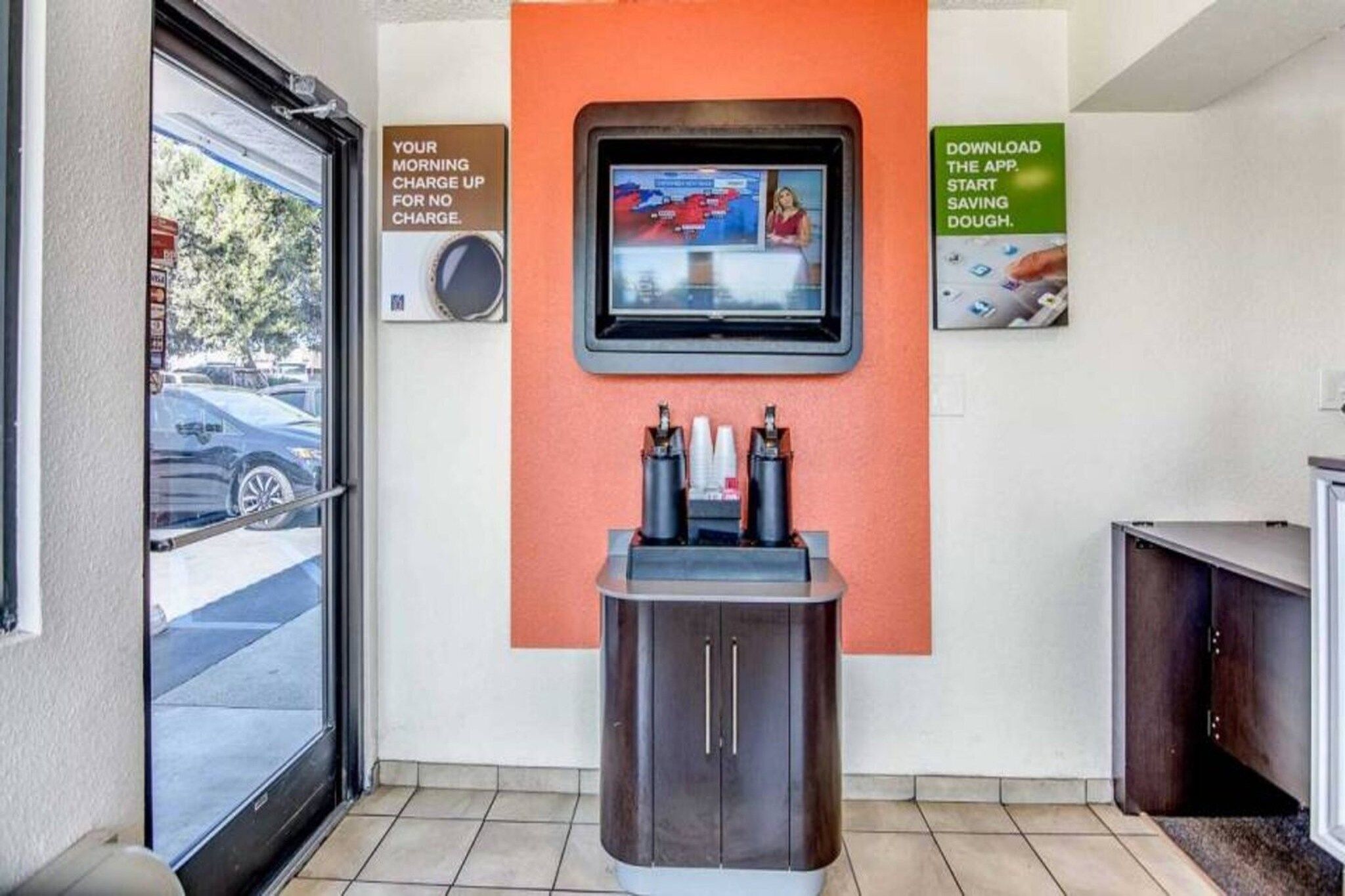Quiosco de autoservicio con pantalla de televisión, estación de carga y un anuncio promocional para una aplicación.