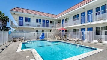 A hotel with a swimming pool, multiple balconies, and a fenced pool area.