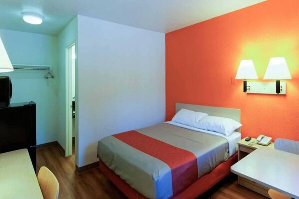 A hotel room with a bed, bedside table, lamp, and a desk with a chair.