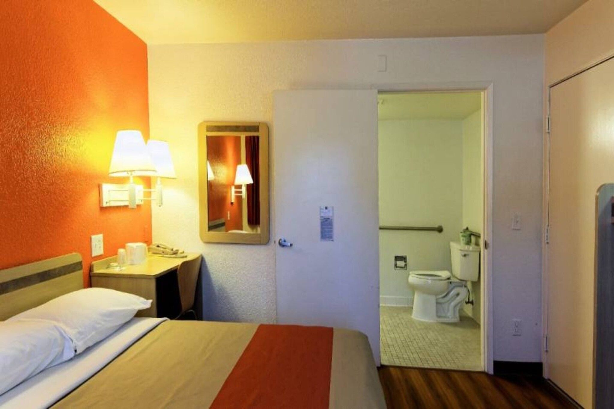 Ein Hotelzimmer mit einem Bett, Nachttischlampen, einem Spiegel und Blick ins Bad.