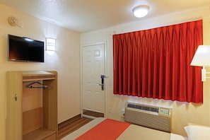 Ein Hotelzimmer mit einem Bett, einem Fernseher, einem Kleiderschrank, einer Tür, einem Fenster mit roten Vorhängen und einer Wand-Klimaanlage.