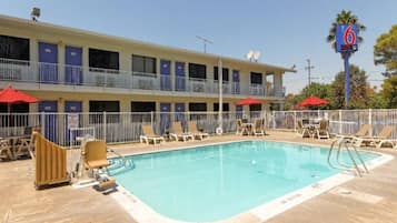 Ein Motel mit Schwimmbad, mehreren Balkonen und roten Sonnenschirmen.