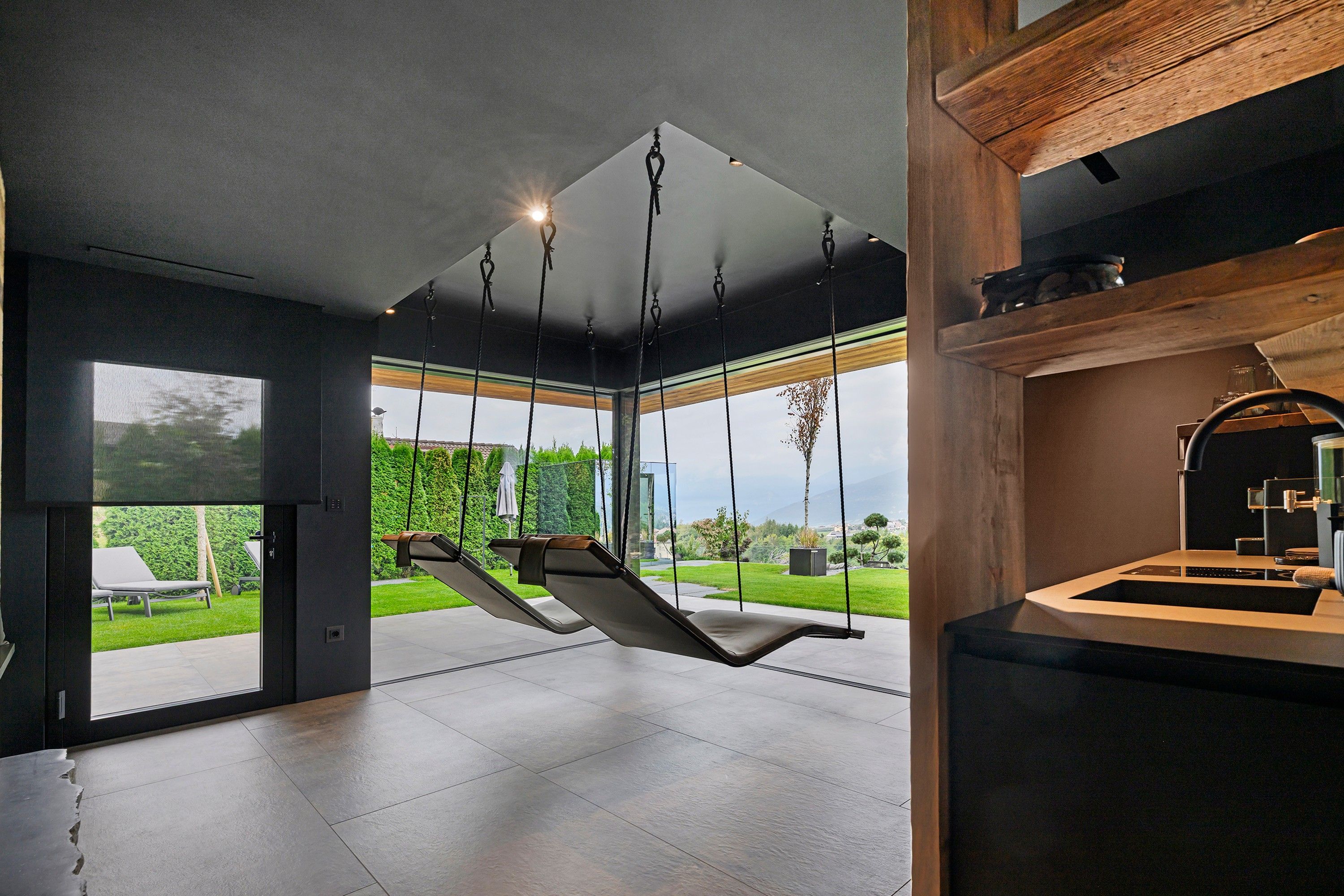 Een modern interieur met een hangstoel, een keukenhoek en uitzicht op een tuin.