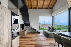 A modern interior with a wooden staircase, a sofa, and a view of the outdoors.