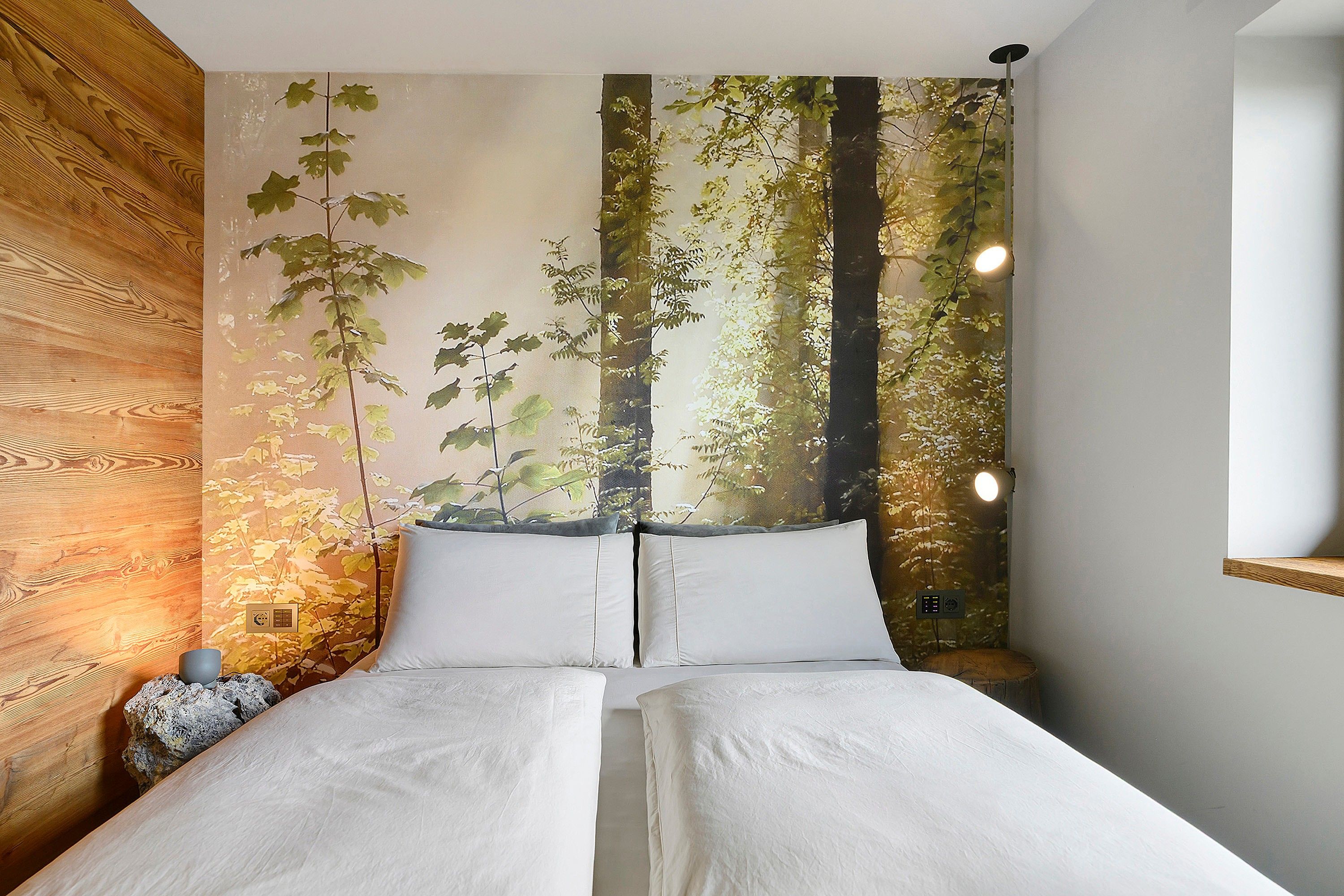 A bedroom with a bed centered between two walls, one with a wooden panel and the other with a forest mural.