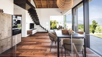 Une cuisine moderne avec un plancher en bois, un coin repas avec une table et des chaises, un escalier et une grande fenêtre donnant sur un paysage verdoyant.