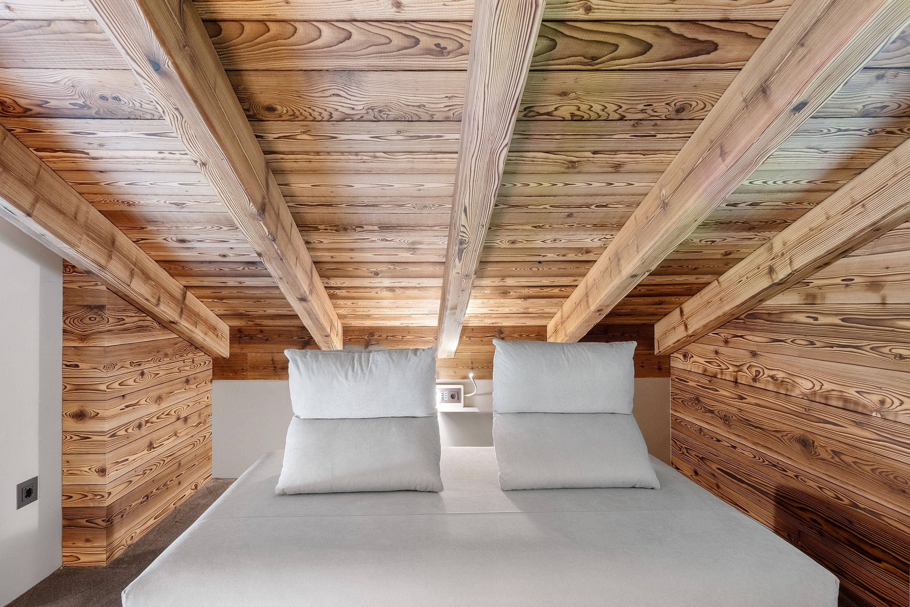 A room with a sloped ceiling and wooden paneling, featuring a bed with two pillows.