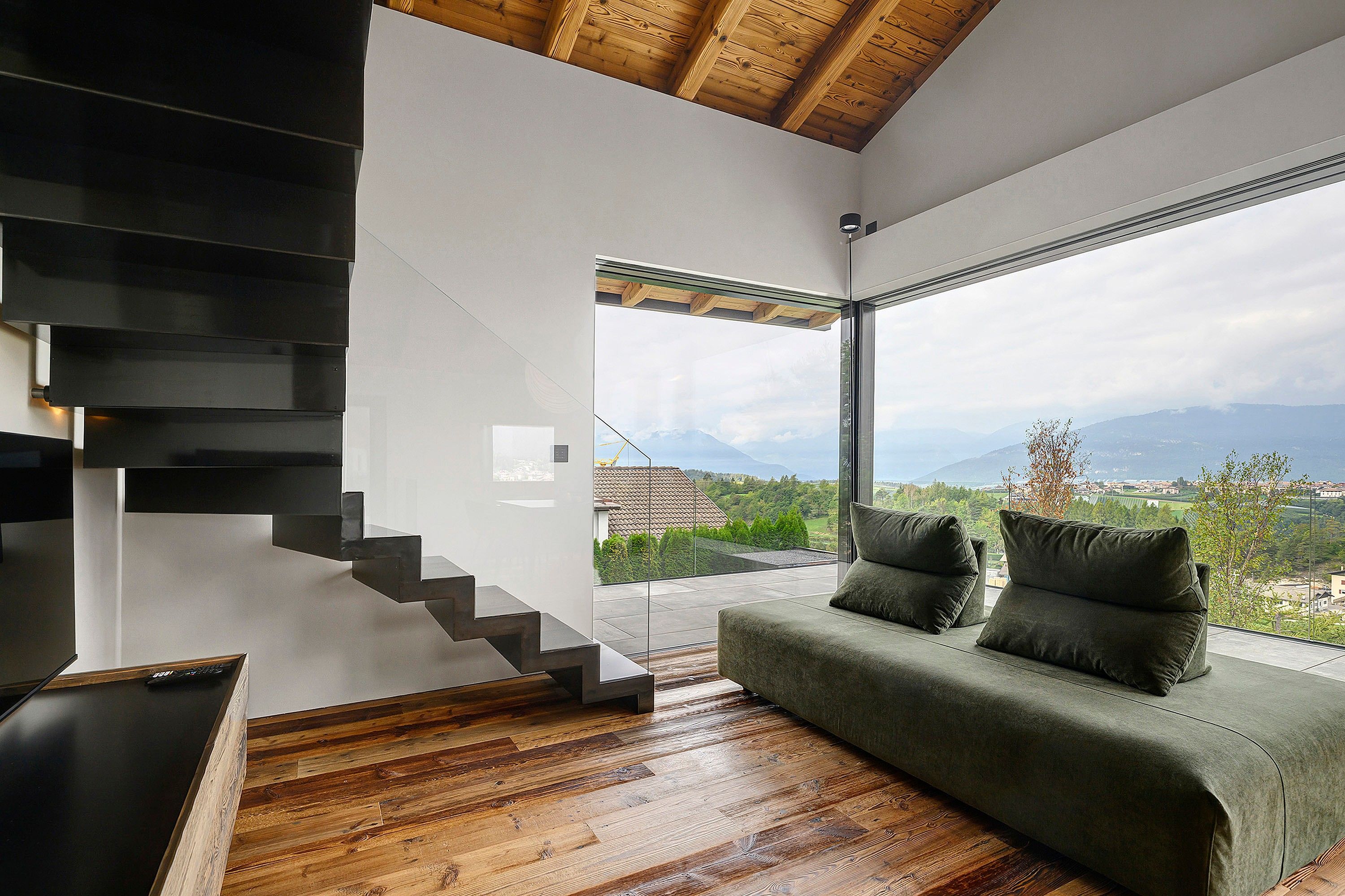A modern interior with a staircase, a green sofa, and a view of a mountainous landscape.