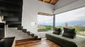 A modern interior with a staircase, a green sofa, and a view of a mountainous landscape.