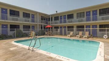 A pool area with a diving board, lounge chairs, and a red umbrella.