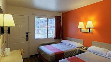 A hotel room with two beds, a desk, a window with a view, and a wall-mounted lamp.