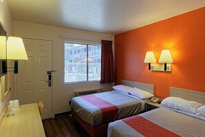 A hotel room with two beds, a desk, a window with a view, and a wall-mounted lamp.