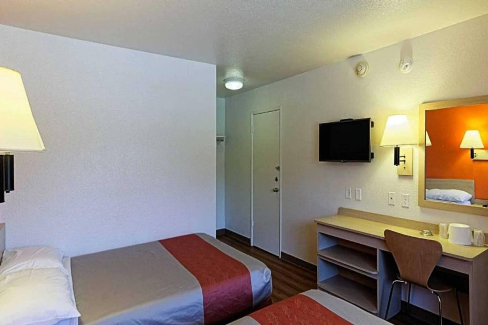Hotellihuone, jossa on kaksi sänkyä, työpöytä, tuoli, televisio ja kylpyhuoneen ovi.