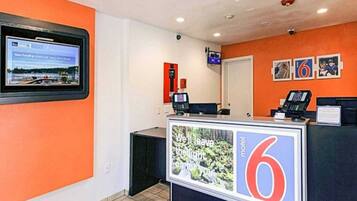 A hotel reception area with a digital screen displaying news, a reception desk with a '6' sign, and a 'motel' sign.