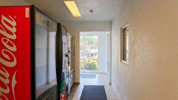 A hallway with a Coca-Cola refrigerator, a water dispenser, and a door leading to a balcony with a view of greenery.