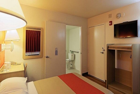A hotel room with a bed, a TV, a bathroom, and a desk with a lamp.