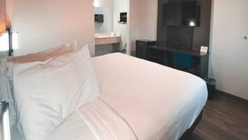 Habitación de hotel con cama, escritorio, espejo y televisión.