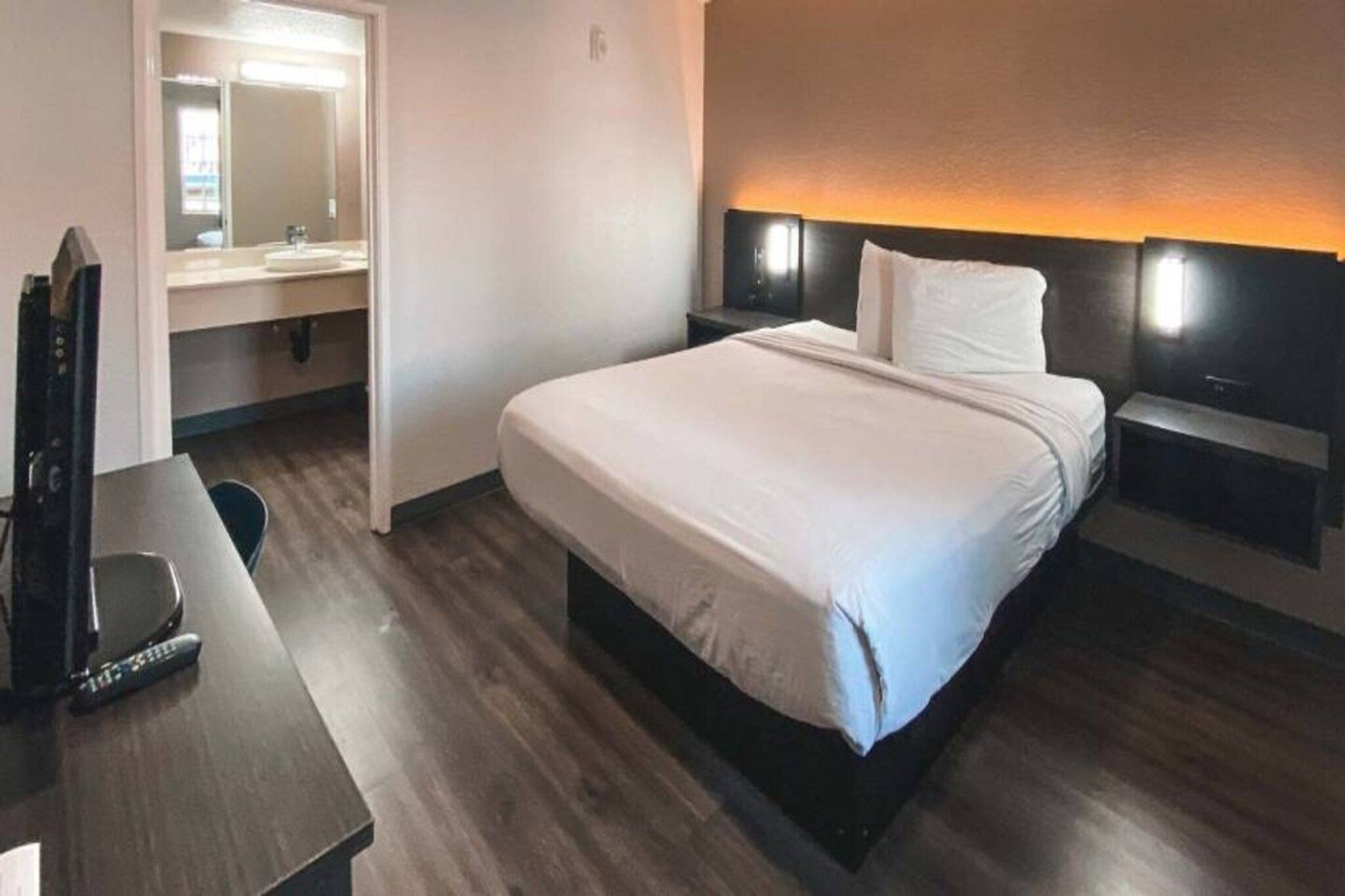 Ein Hotelzimmer mit einem Bett, Nachttischen, einem Schreibtisch mit Stuhl, einem Spiegel und einer Wandleuchte.