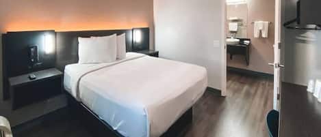 A hotel room with a bed, bedside tables, a TV, and a bathroom visible through an open door.
