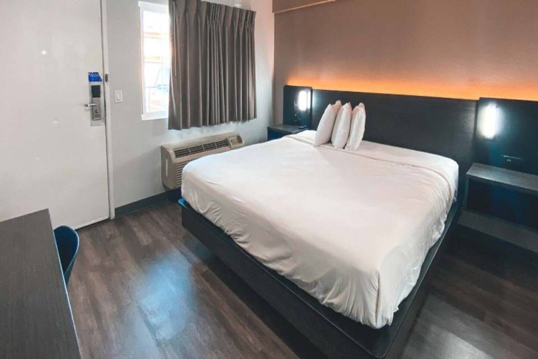 Habitación de hotel con una cama grande, un escritorio, una silla, un equipo de aire acondicionado y una ventana con cortinas.