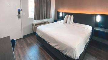 Habitación de hotel con una cama grande, un escritorio, una silla, un equipo de aire acondicionado y una ventana con cortinas.