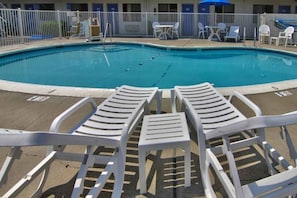 Piscina con sillas de descanso y mesas, rodeada por una cerca.