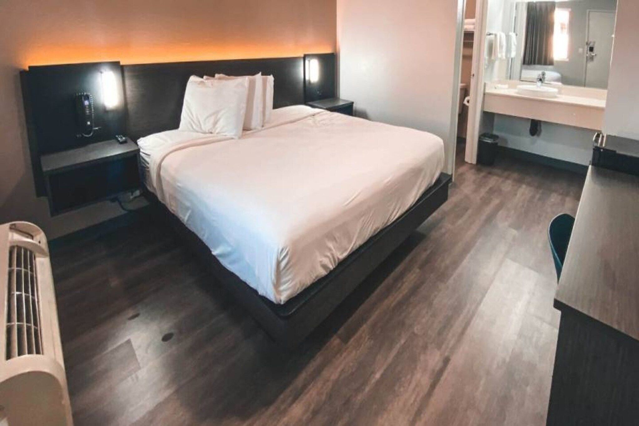 Quarto de hotel moderno com uma cama grande, mesas de cabeceira, aquecedor embutido, espelho e um pequeno espaço para sentar.