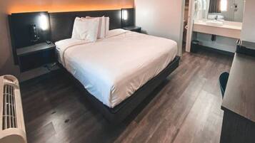 Quarto de hotel moderno com uma cama grande, mesas de cabeceira, aquecedor embutido, espelho e um pequeno espaço para sentar.