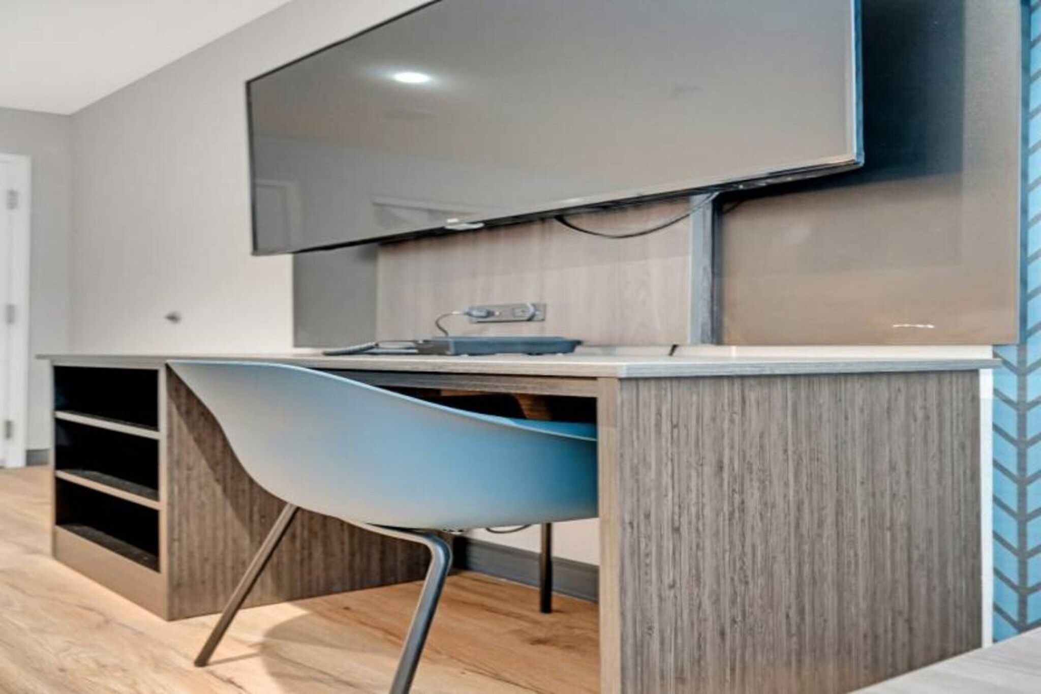 A modern room with a flat-screen TV mounted on the wall, a wooden desk with a chair, and a built-in shelving unit.