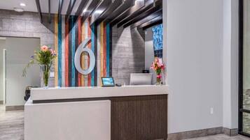 A reception desk with a large number '6' sign, a laptop, and two vases with flowers.