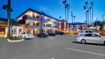 A multi-story hotel with a parking lot, several cars, and palm trees.
