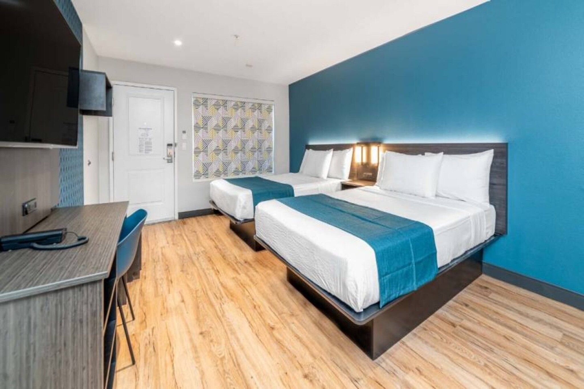 A hotel room with two beds, a desk, and a TV.